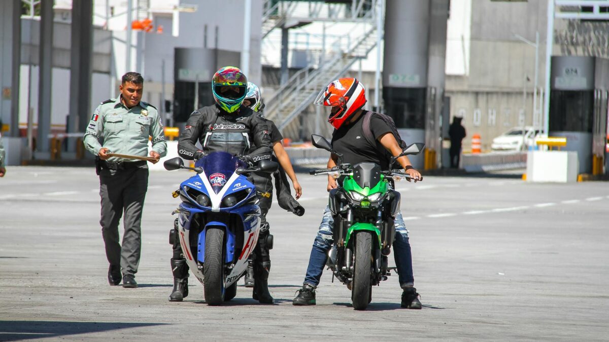 Führerschein kosten – Erstes Auto & Führerschein (Symbolbild: Motorradfahrer mit Helmen interagieren an einem Grenzkontrollpunkt im Freien mit einem Polizisten.)