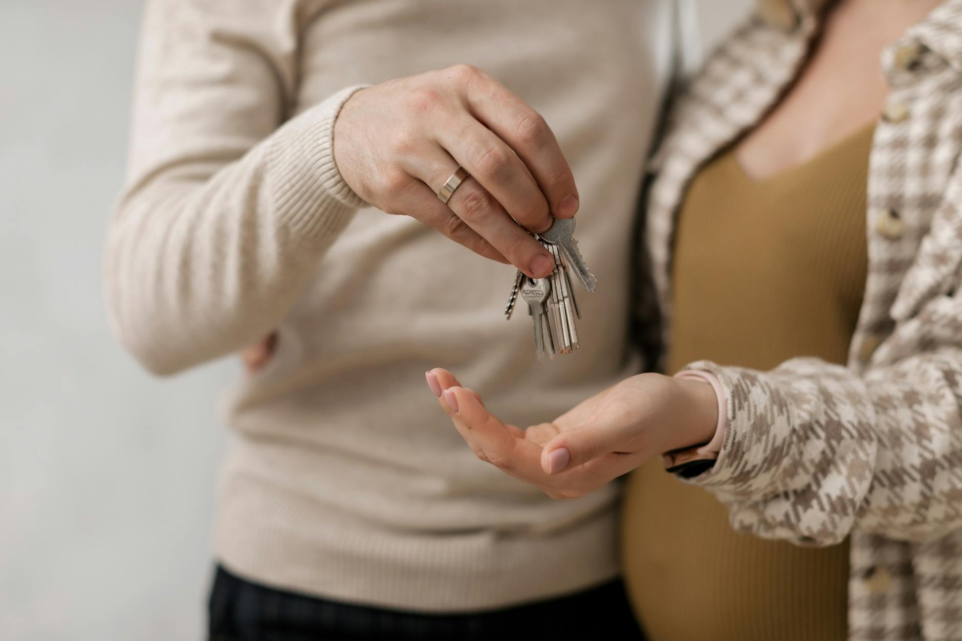 Eine Hand übergibt einen Schlüsselbund an eine andere Hand vor einer unscharfen Wohnungstür.