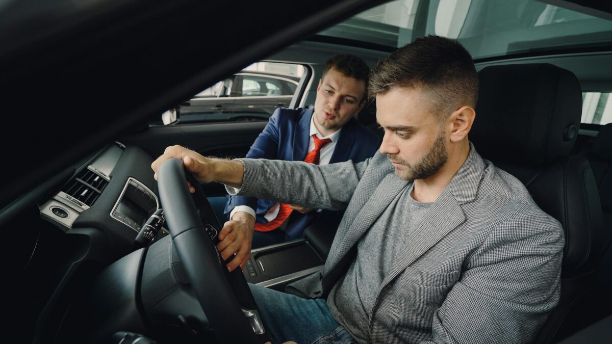 Jahreswagen kaufen – Erstes Auto & Führerschein (Symbolbild: Verkäufer demonstriert potenziellen Käufern die Fahrzeugmerkmale im Fahrzeugausstellungsraum.)