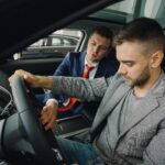 Jahreswagen kaufen – Erstes Auto & Führerschein (Symbolbild: Verkäufer demonstriert potenziellen Käufern die Fahrzeugmerkmale im Fahrzeugausstellungsraum.)
