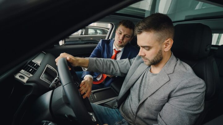 Jahreswagen kaufen – Erstes Auto & Führerschein (Symbolbild: Verkäufer demonstriert potenziellen Käufern die Fahrzeugmerkmale im Fahrzeugausstellungsraum.)