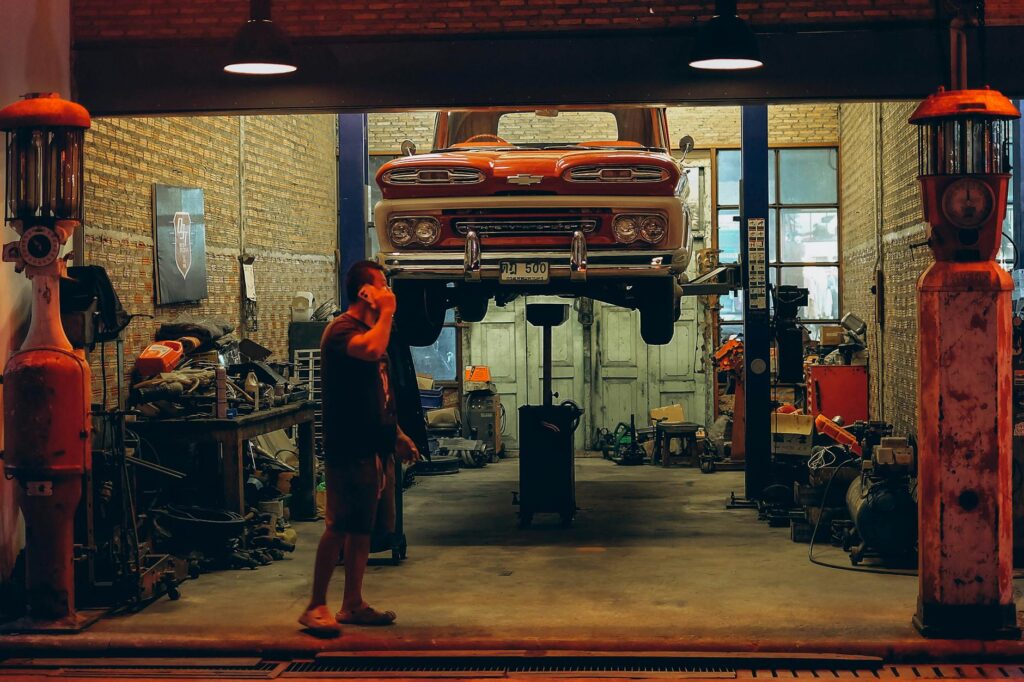 Kfz versicherung fahranfänger – Erstes Auto & Führerschein (Symbolbild: In einer Garage in Bangkok wird ein roter Oldtimer-Lkw angehoben. Industrielles Ambiente mit nostalgischen Automobil-Elementen.)