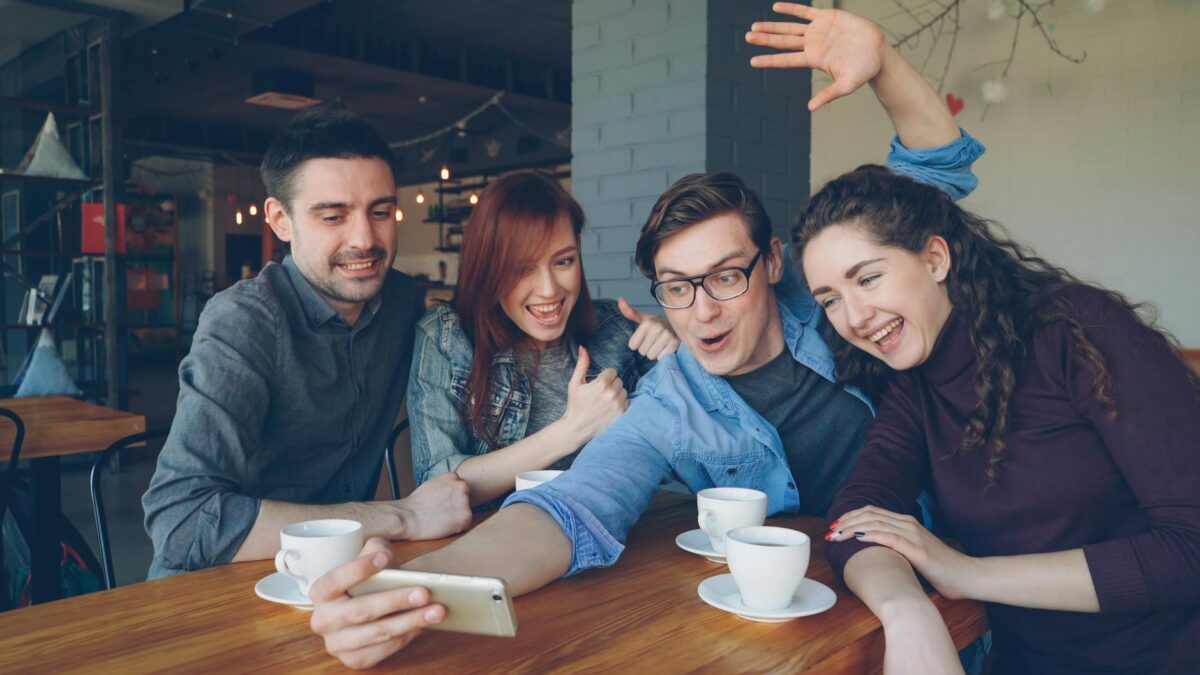 Privathaftpflicht junge erwachsene – Erste eigene Versicherung (Symbolbild: Eine Gruppe von Freunden hat Spaß, trinkt Kaffee und macht ein Selfie in einem Café.)
