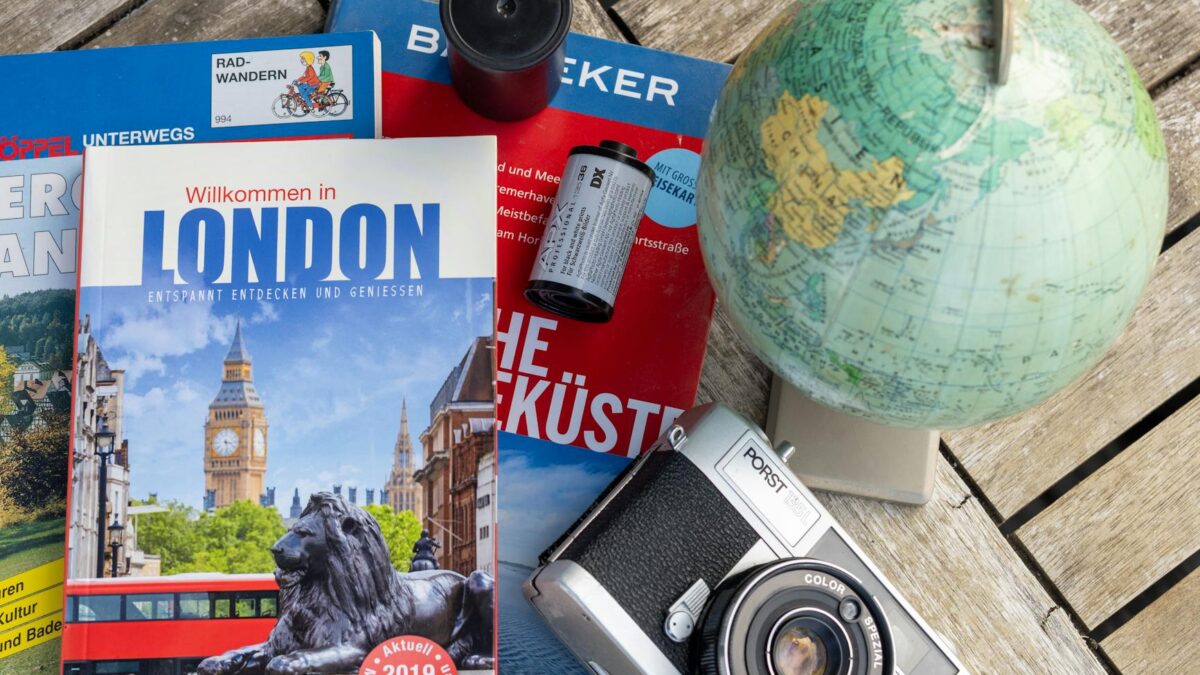 Reise stornieren – Erste Reise allein (Symbolbild: Flaches Layout mit London-Reiseführer, Vintage-Kamera und Globus, ideal für Reisethemen.)