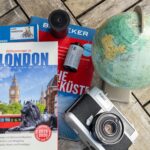 Reise stornieren – Erste Reise allein (Symbolbild: Flaches Layout mit London-Reiseführer, Vintage-Kamera und Globus, ideal für Reisethemen.)