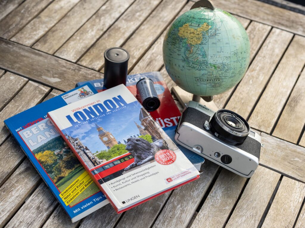 Reise stornieren – Erste Reise allein (Symbolbild: Eine Vintage-Reiseausstattung mit Reiseführern, einem Globus und einer Filmkamera auf einem Holztisch.)